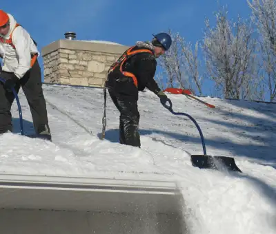 Professional technicians performing roof snow removal with safety harnesses and shovels in Little Rock, AR